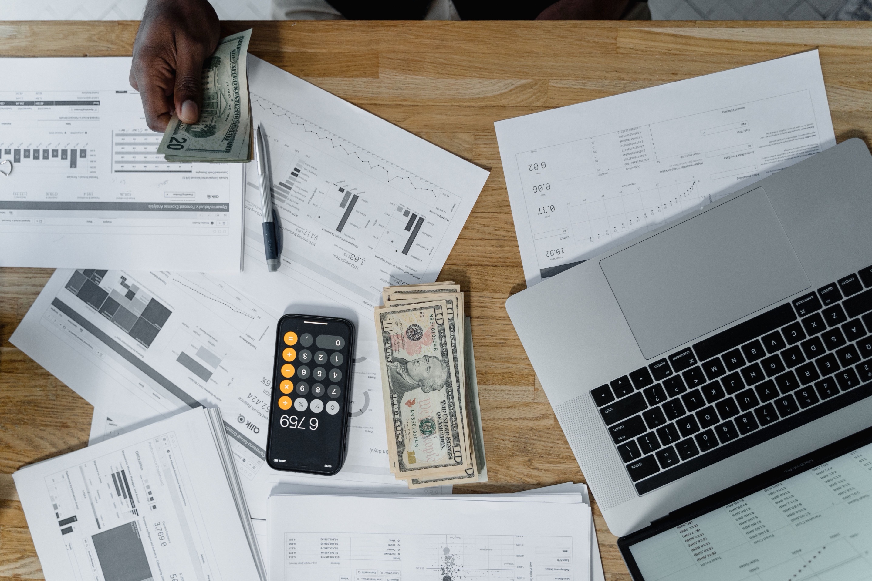 Overhead view of cash, a calculator, financial reports, and a laptop during tax reconciliation